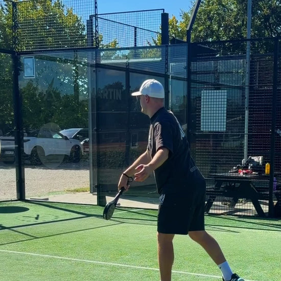 A player hitting a serve with the JURO FOCUS on an outdoor padel court