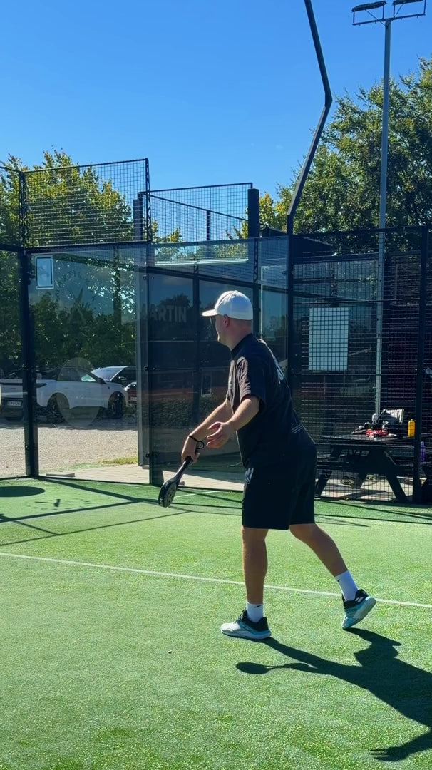 A player hitting a serve with the JURO FOCUS on an outdoor padel court